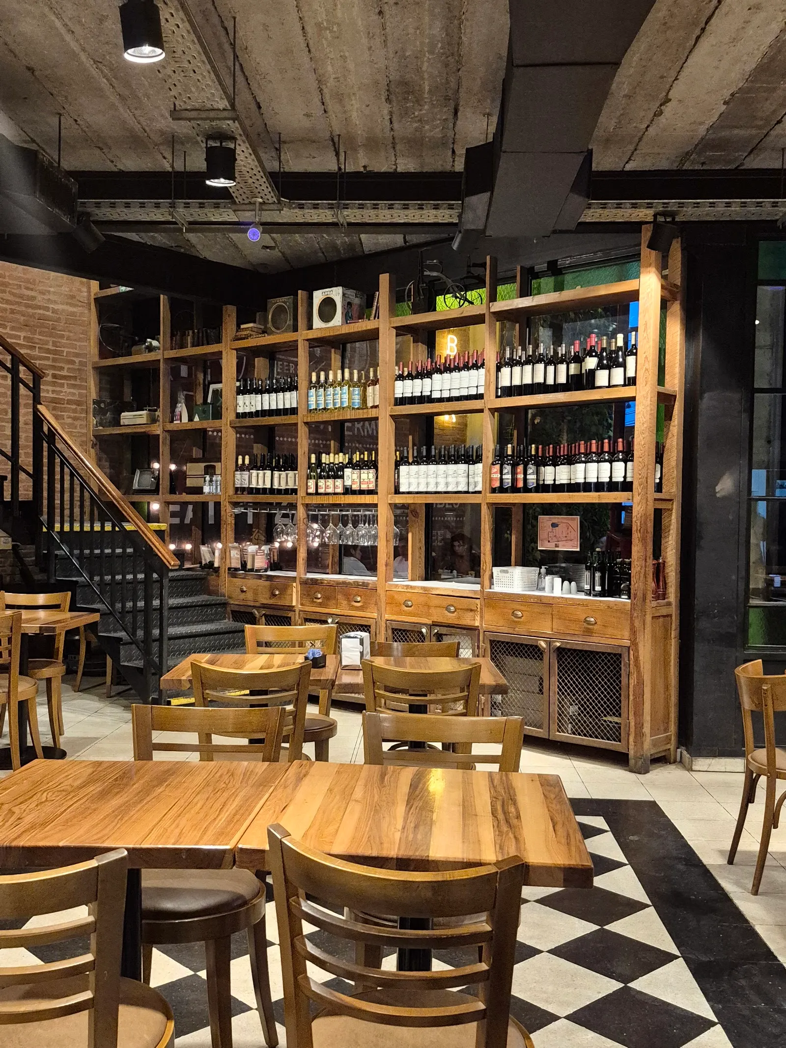 Salón de Biblos con estantería de vinos, mesas de madera y piso damero