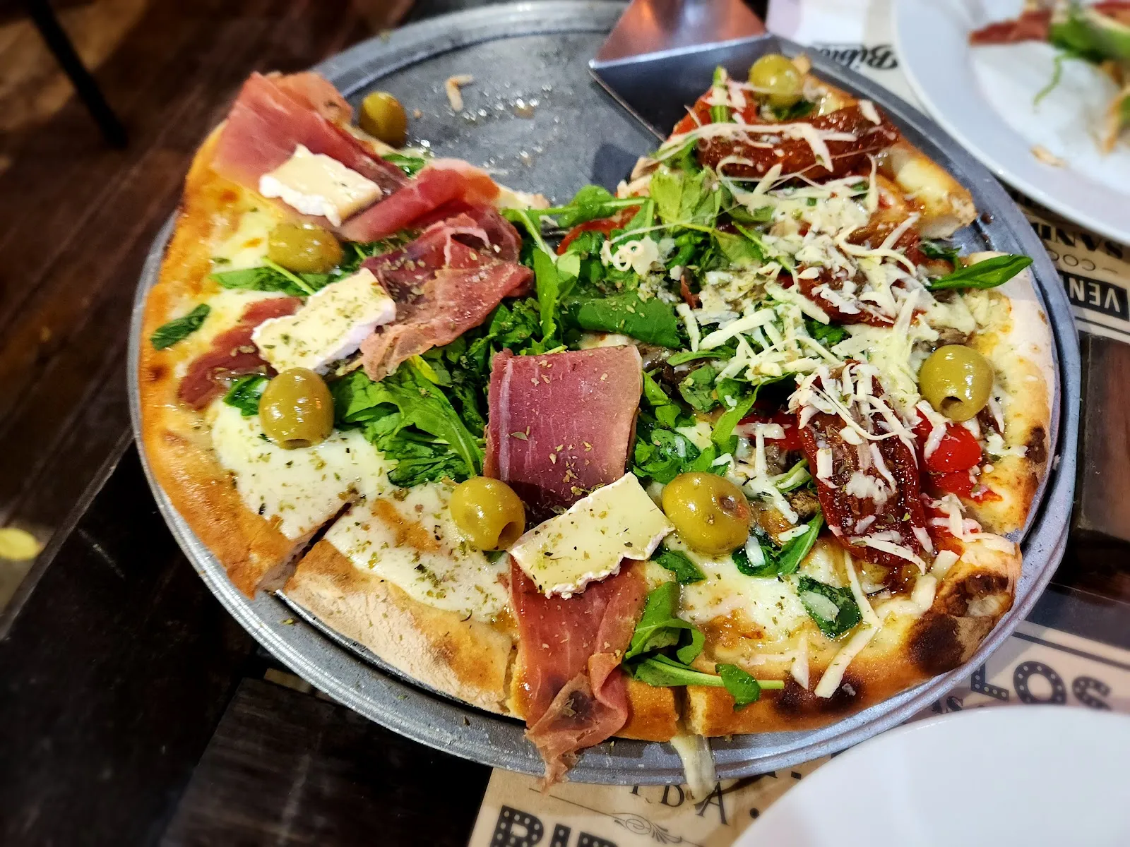 Pizza a la piedra con rúcula, jamón crudo, brie y aceitunas